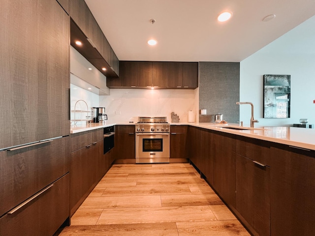 kitchen with light wood-style flooring, a sink, light countertops, high end appliances, and modern cabinets