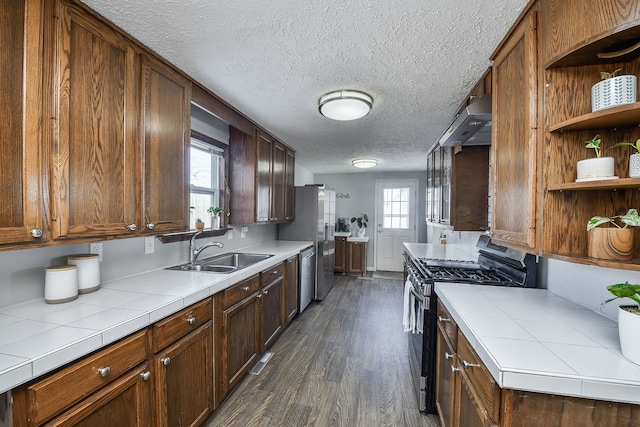 kitchen featuring sink, a textured ceiling, appliances with stainless steel finishes, tile counters, and dark hardwood / wood-style flooring