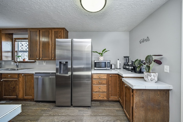 kitchen with appliances with stainless steel finishes, sink, dark wood-type flooring, and a textured ceiling