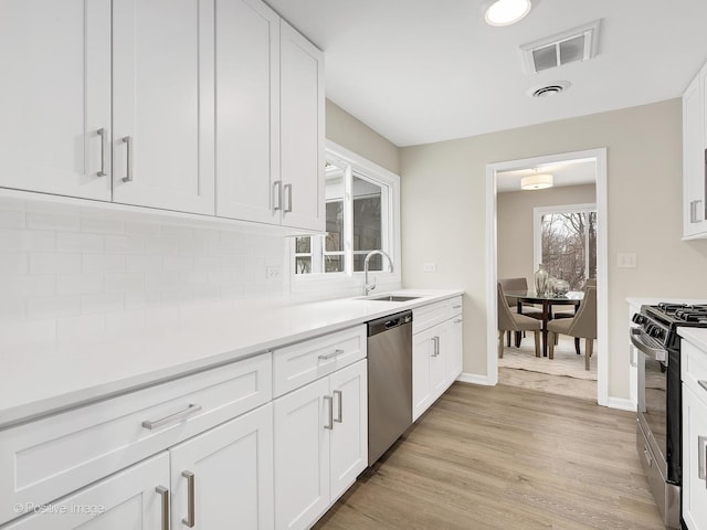 kitchen with sink, gas range, light hardwood / wood-style flooring, dishwasher, and white cabinets