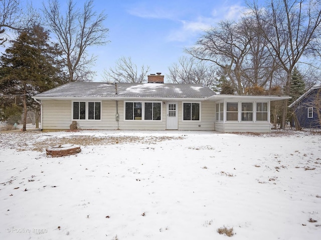 snow covered back of property with a sunroom