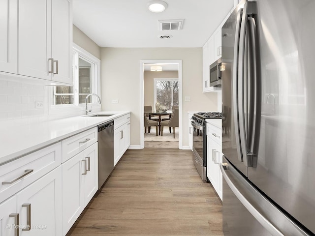 kitchen featuring sink, white cabinets, decorative backsplash, stainless steel appliances, and light wood-type flooring