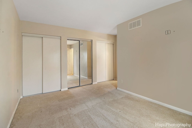 unfurnished bedroom featuring multiple closets and light colored carpet