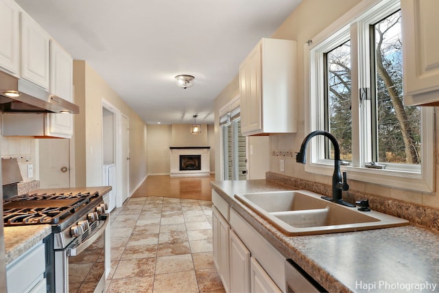 kitchen with gas range, a fireplace, sink, and white cabinets