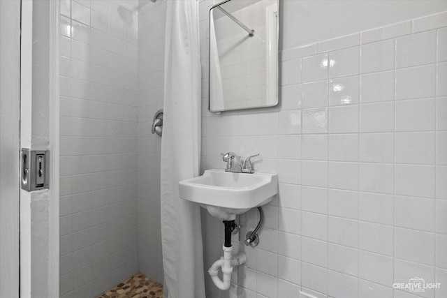 bathroom with sink, a tile shower, and tile walls