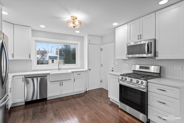 kitchen featuring appliances with stainless steel finishes, sink, white cabinets, decorative backsplash, and dark wood-type flooring