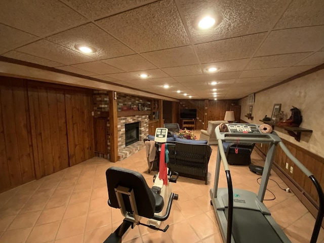 exercise room featuring a drop ceiling, a fireplace, and wood walls