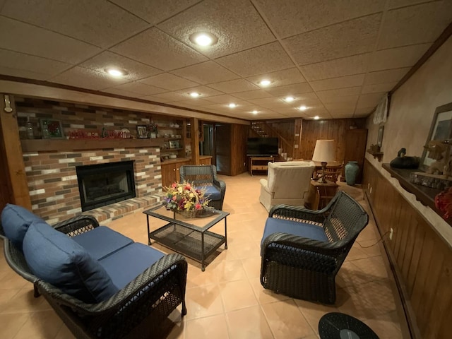 tiled living room featuring a drop ceiling, a fireplace, built in features, and wooden walls