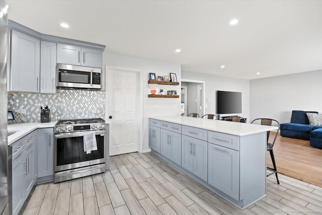 kitchen with a kitchen bar, appliances with stainless steel finishes, kitchen peninsula, gray cabinets, and backsplash