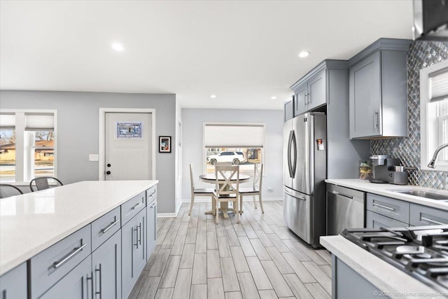 kitchen with sink, light wood-type flooring, gray cabinets, stainless steel appliances, and decorative backsplash