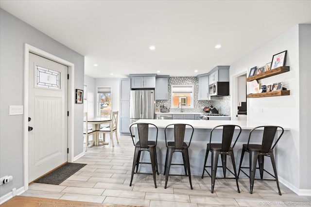 kitchen featuring stainless steel appliances, gray cabinetry, a kitchen bar, and kitchen peninsula