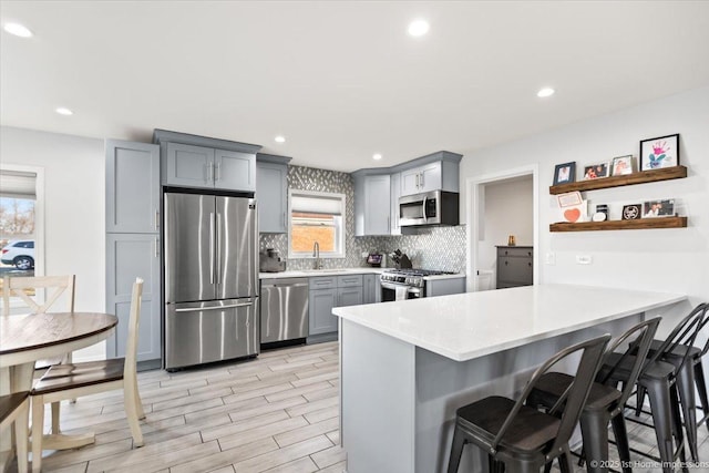 kitchen featuring sink, gray cabinetry, stainless steel appliances, a kitchen bar, and kitchen peninsula