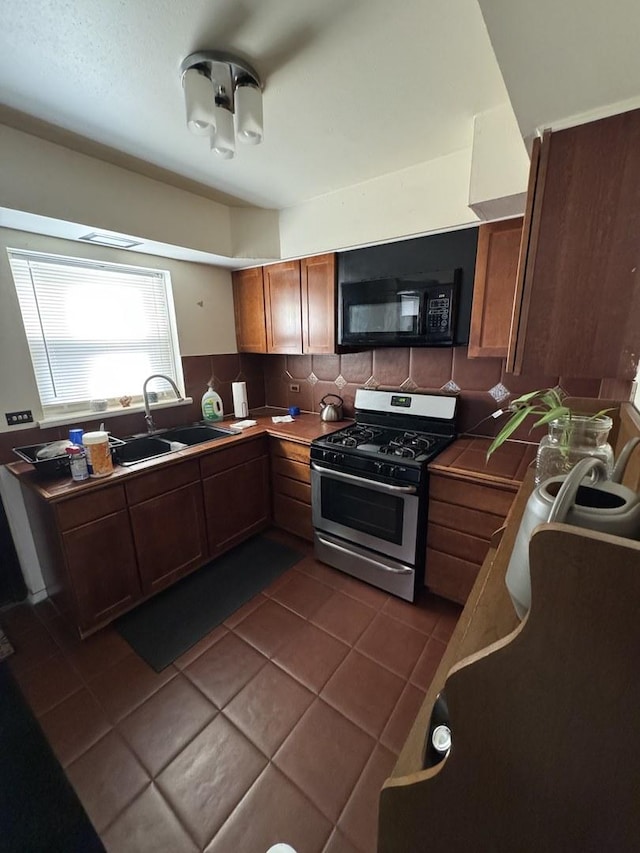 kitchen with sink, decorative backsplash, stainless steel gas range, and dark tile patterned floors