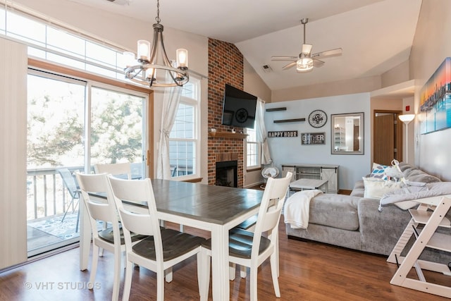 dining room with dark wood-type flooring, ceiling fan with notable chandelier, vaulted ceiling, and a brick fireplace