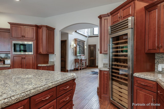 kitchen with backsplash, light stone counters, light hardwood / wood-style floors, built in microwave, and beverage cooler