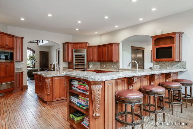 kitchen with light stone counters, stainless steel microwave, light hardwood / wood-style floors, decorative backsplash, and kitchen peninsula