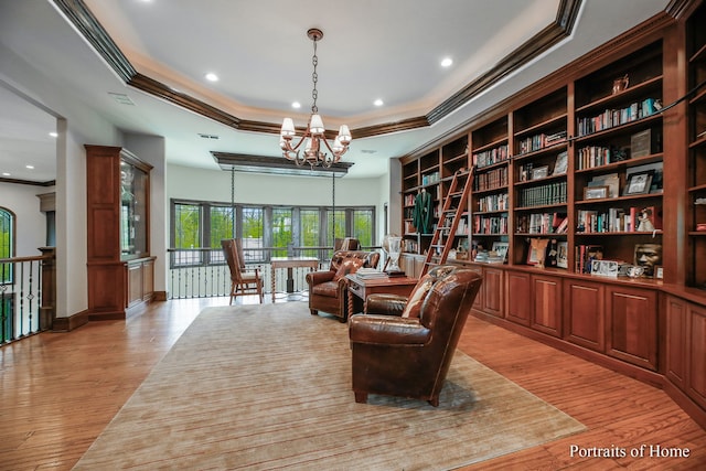 living area with crown molding, a tray ceiling, a chandelier, and light wood-type flooring