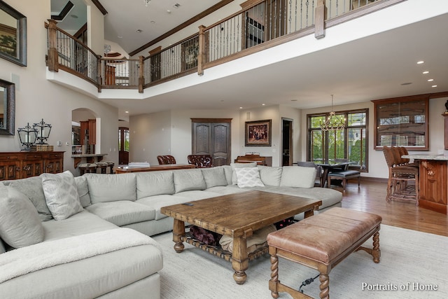 living room with hardwood / wood-style flooring, crown molding, an inviting chandelier, and a high ceiling