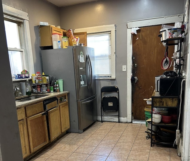 kitchen with stainless steel refrigerator with ice dispenser, sink, a wealth of natural light, and light tile patterned floors