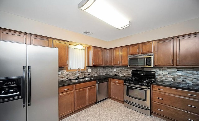 kitchen with stainless steel appliances, sink, decorative backsplash, and dark stone counters