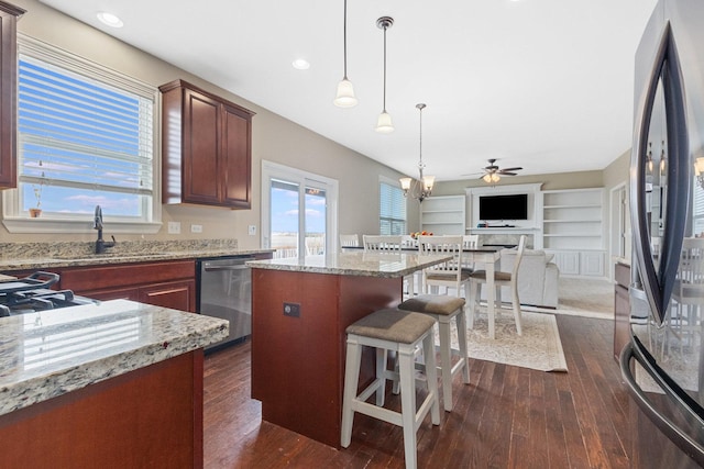 kitchen with appliances with stainless steel finishes, sink, hanging light fixtures, light stone counters, and dark wood-type flooring