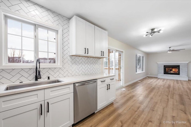 kitchen with a fireplace, tasteful backsplash, white cabinetry, dishwasher, and sink