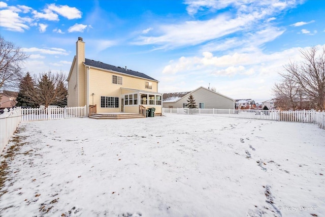 snow covered back of property featuring a sunroom