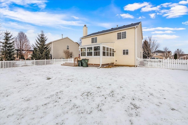 snow covered rear of property featuring a sunroom