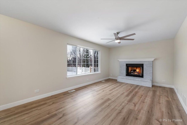 unfurnished living room with a brick fireplace, ceiling fan, and light wood-type flooring