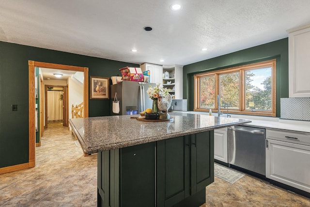 kitchen with appliances with stainless steel finishes, white cabinetry, a center island, light stone countertops, and a textured ceiling