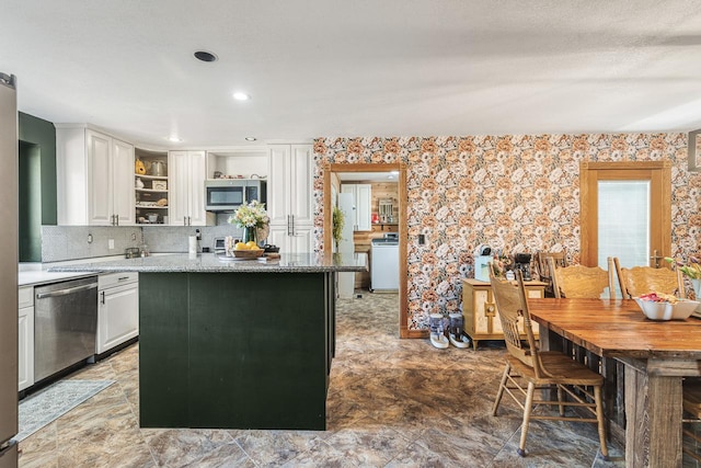 kitchen featuring appliances with stainless steel finishes, light stone countertops, white cabinets, washer / clothes dryer, and decorative backsplash