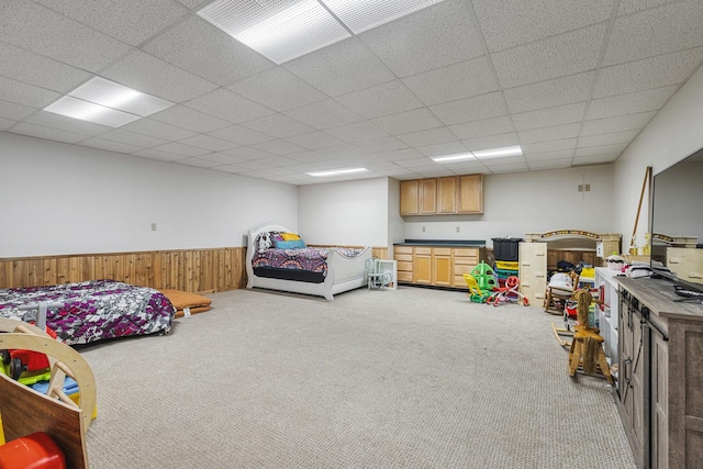 bedroom with wooden walls, light carpet, and a drop ceiling