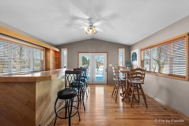 dining room featuring ceiling fan, indoor bar, lofted ceiling, and light hardwood / wood-style flooring