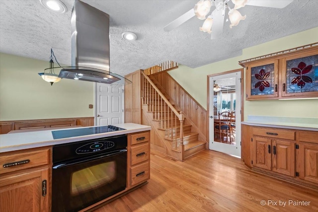 kitchen with ceiling fan, island range hood, black appliances, a textured ceiling, and light wood-type flooring