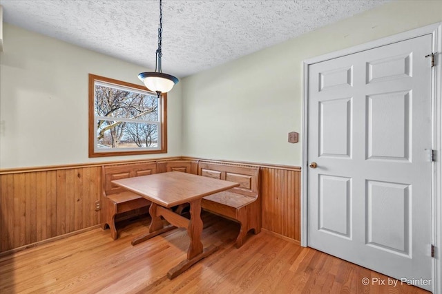 dining room featuring breakfast area, wooden walls, light hardwood / wood-style floors, and a textured ceiling