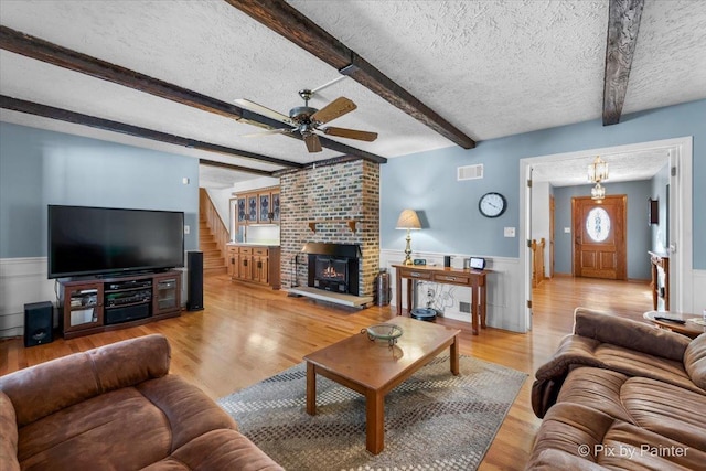 living room featuring ceiling fan, beam ceiling, a fireplace, a textured ceiling, and light wood-type flooring