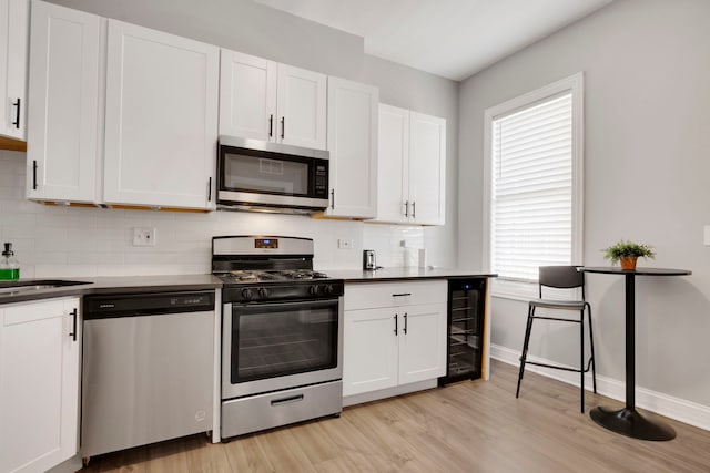 kitchen with tasteful backsplash, white cabinets, beverage cooler, stainless steel appliances, and light hardwood / wood-style flooring