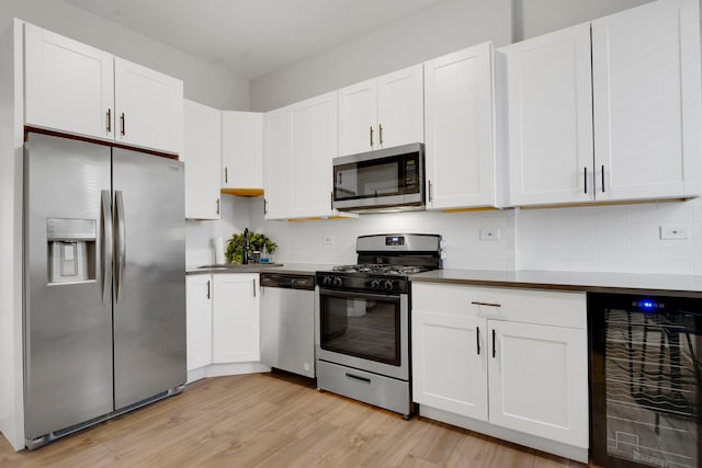 kitchen featuring appliances with stainless steel finishes, white cabinetry, beverage cooler, backsplash, and light hardwood / wood-style floors