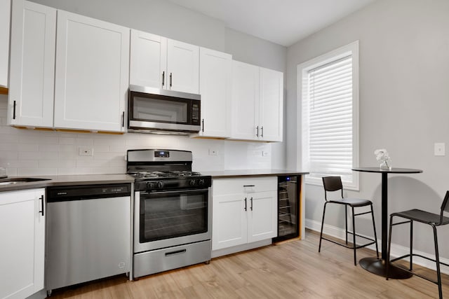 kitchen featuring appliances with stainless steel finishes, white cabinetry, wine cooler, tasteful backsplash, and light wood-type flooring