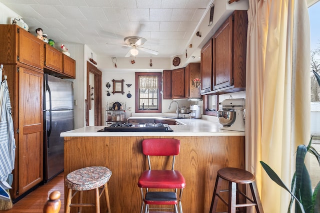 kitchen featuring black gas cooktop, sink, stainless steel fridge, a kitchen bar, and kitchen peninsula