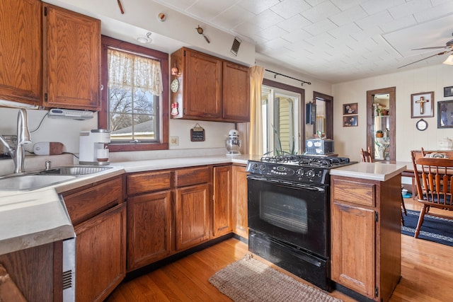 kitchen featuring sink, ceiling fan, black gas stove, light hardwood / wood-style floors, and kitchen peninsula