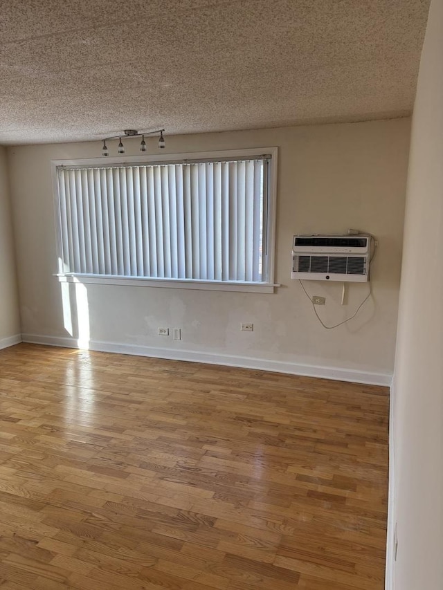 empty room featuring track lighting, hardwood / wood-style floors, a wall unit AC, and a textured ceiling