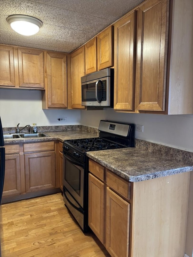 kitchen with appliances with stainless steel finishes, sink, light hardwood / wood-style flooring, and a textured ceiling