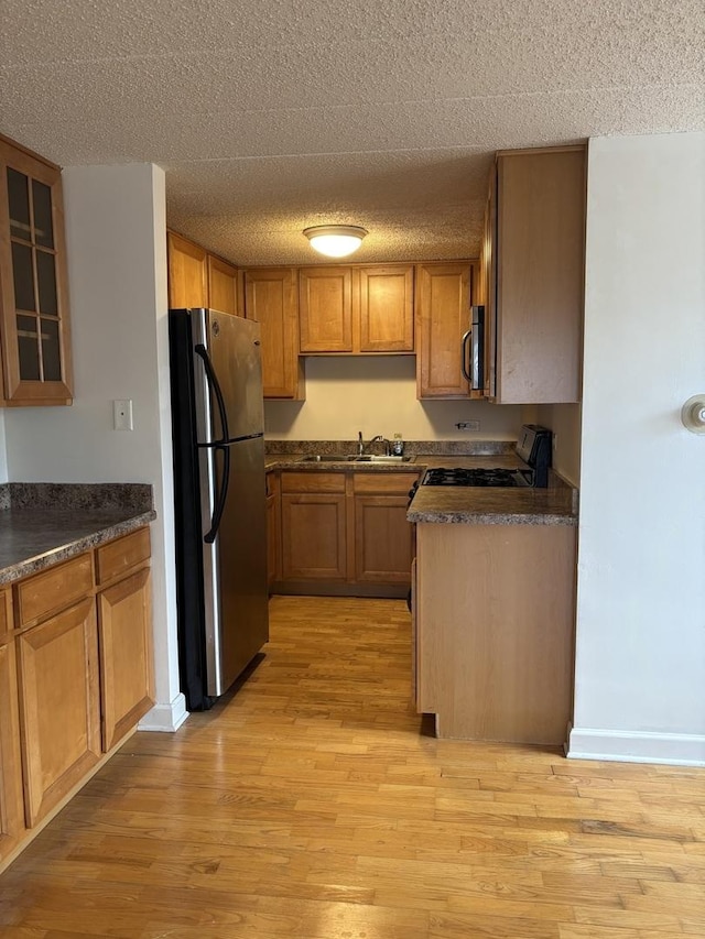 kitchen with appliances with stainless steel finishes, sink, a textured ceiling, and light hardwood / wood-style flooring