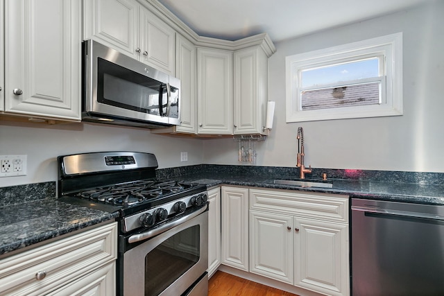 kitchen with sink, stainless steel appliances, dark stone counters, and white cabinets