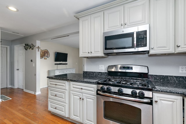 kitchen featuring white cabinetry, stainless steel appliances, light hardwood / wood-style flooring, and dark stone counters