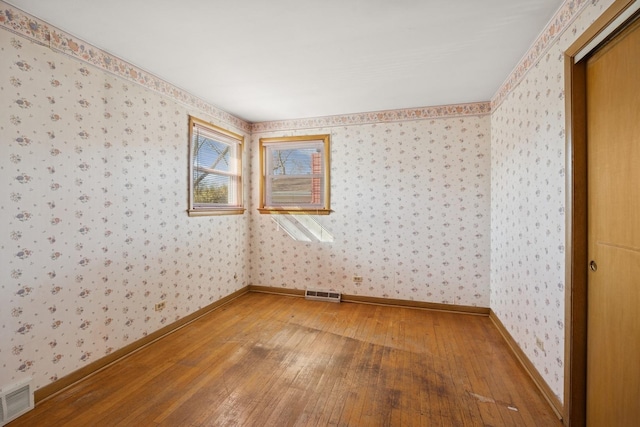 spare room with hardwood / wood-style flooring, visible vents, and wallpapered walls