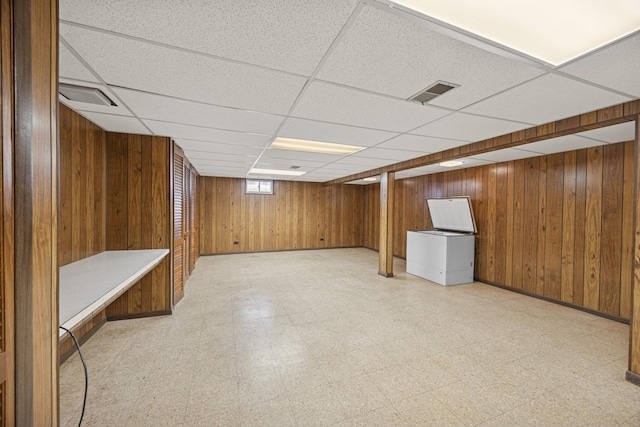 below grade area featuring light floors, a paneled ceiling, wood walls, and visible vents