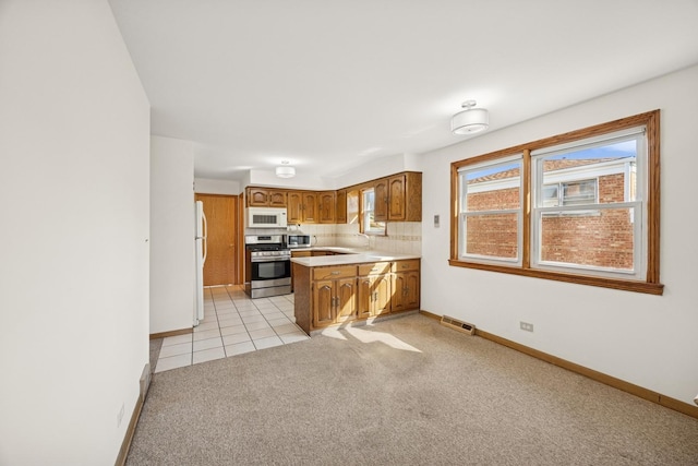 kitchen featuring brown cabinets, light colored carpet, visible vents, appliances with stainless steel finishes, and a peninsula