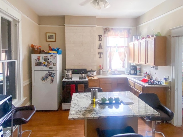 kitchen featuring light stone counters, range, light wood-type flooring, a kitchen island, and white fridge